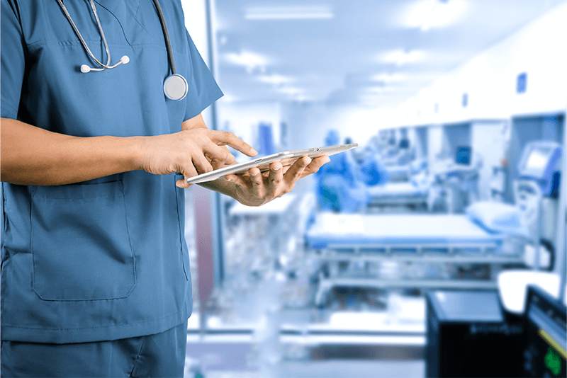 nurse tapping ipad while standing in front of medical beds
