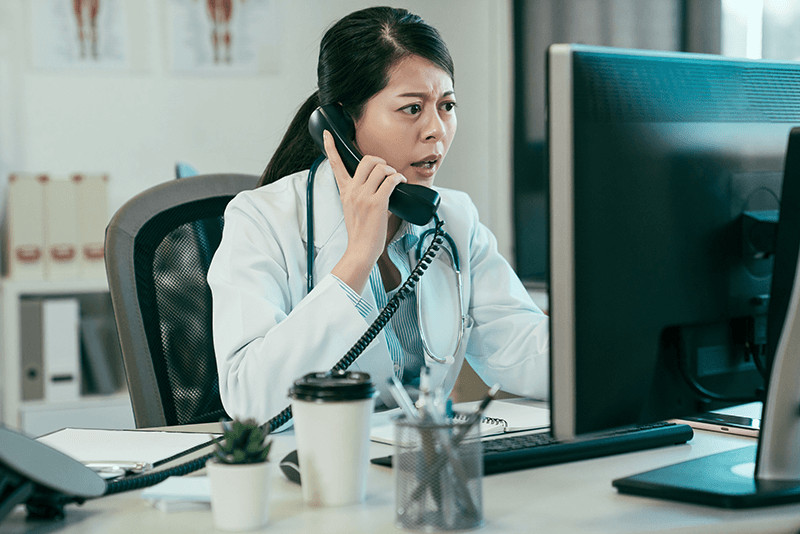 angry doctor looking at computer monitor while on the phone
