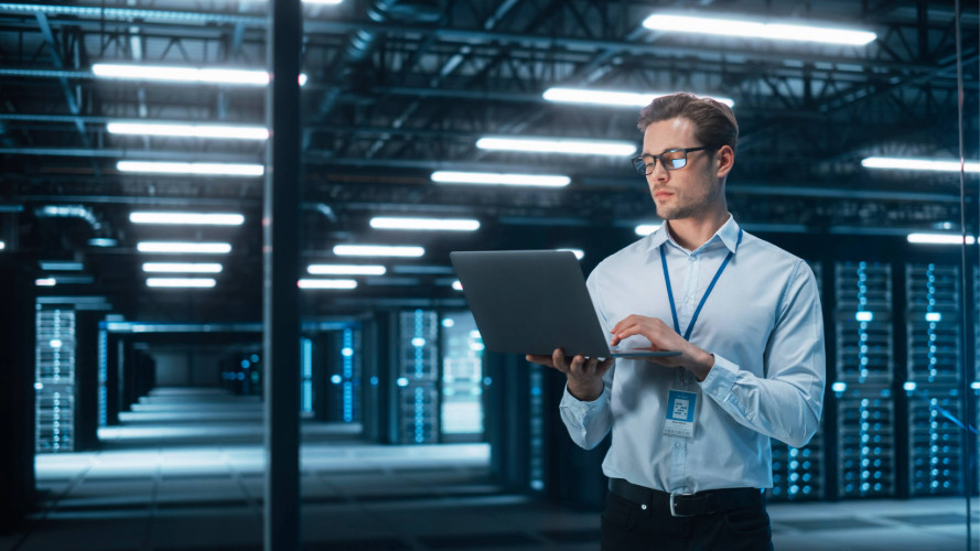IT man standing in data center with laptop.